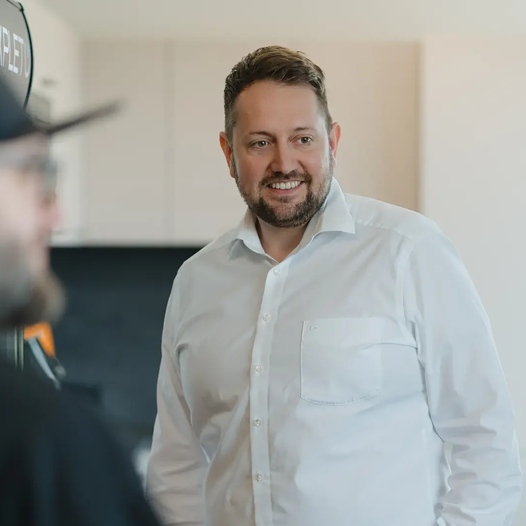 Lächelnder EXPLETO-Mitarbeiter im persönlichen Austausch mit Kollegen in einer hellen, modernen Büroumgebung.
