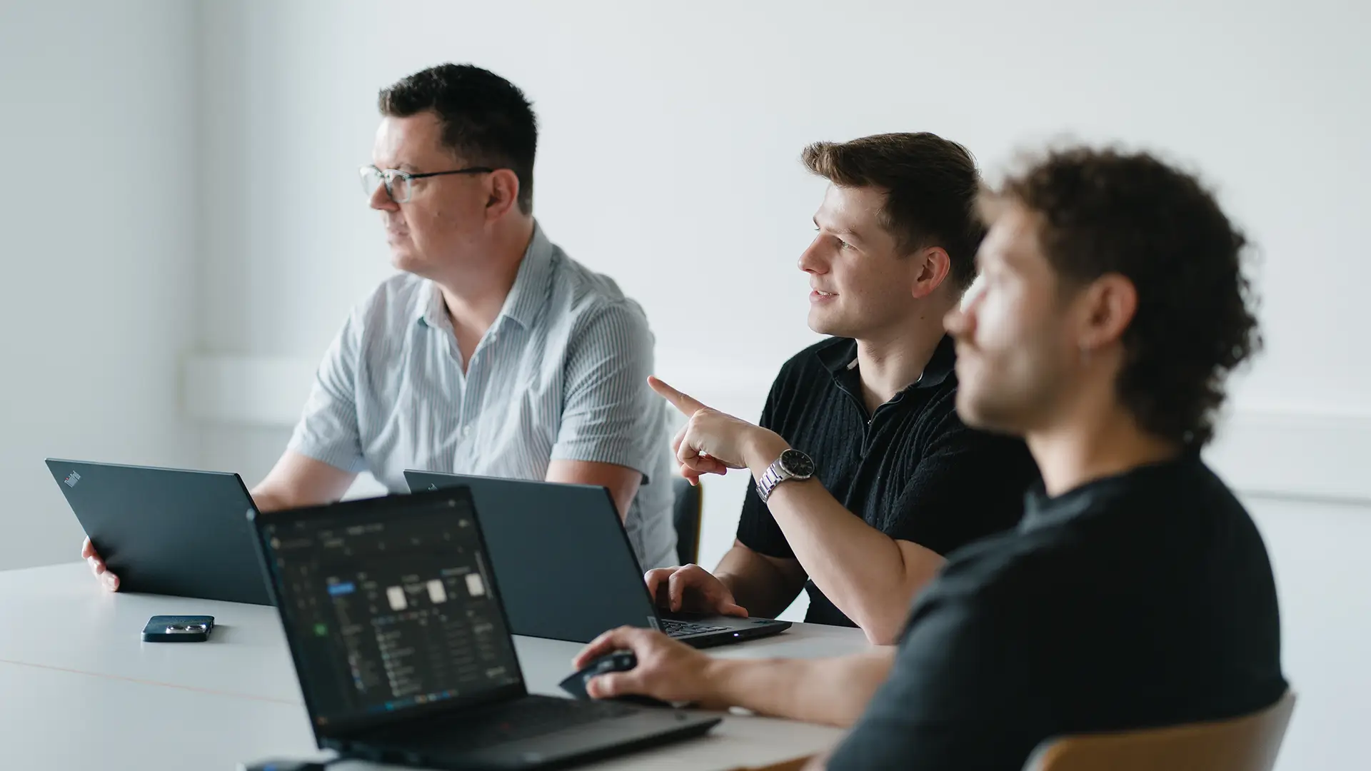 Drei EXPLETO-Mitarbeiter arbeiten gemeinsam an Laptops und tauschen sich während einer IT-Besprechung konzentriert über digitale Lösungen und Projekte aus.