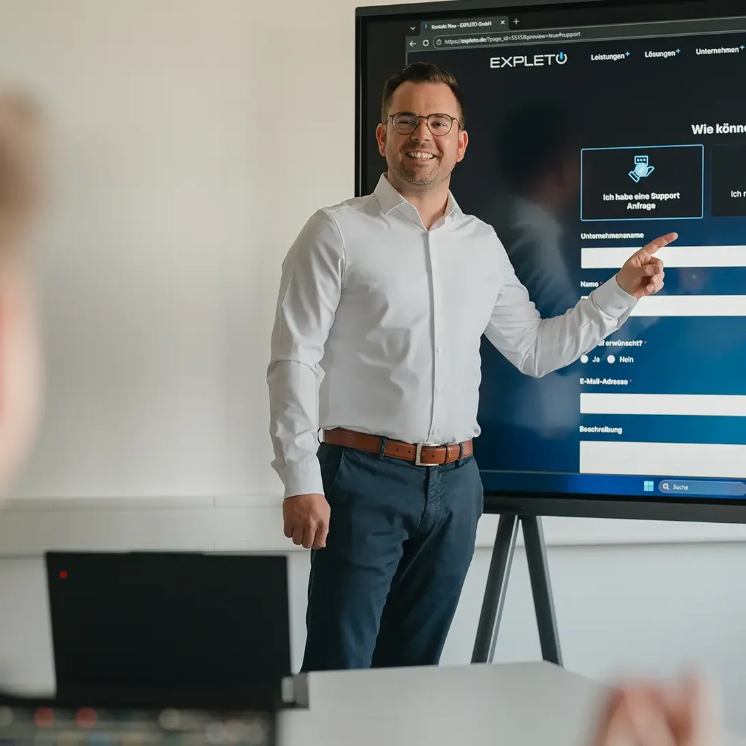 Mitarbeiter präsentiert die digitale Support- und Serviceplattform von EXPLETO auf einem großen Bildschirm während einer Besprechung im Büro.