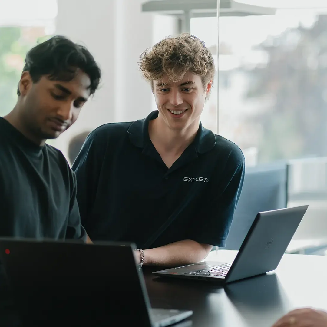 Drei EXPLETO-Mitarbeiter arbeiten gemeinsam an Laptops und tauschen sich in einer hellen, modernen Büroumgebung zu einem Projekt aus.