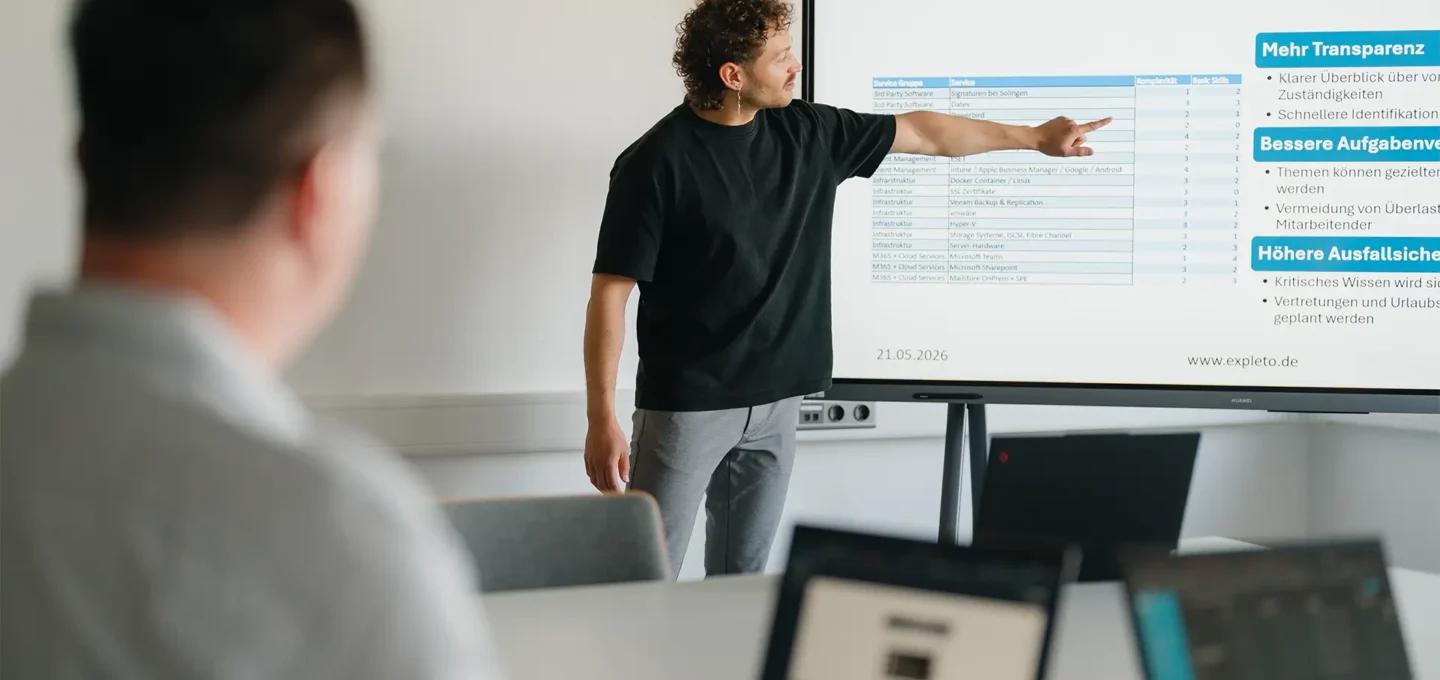 EXPLETO-Mitarbeiter präsentiert die Einführung einer Skillmatrix auf einem großen Bildschirm und erläutert die Vorteile für Transparenz, Aufgabenverteilung und Wissensmanagement im Team.